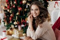 Portrait of a beautiful woman with curls at the Christmas tree with gifts of new year lights garland