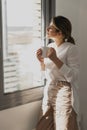 Young beautiful woman near window with cup of coffee or tea at home. Royalty Free Stock Photo