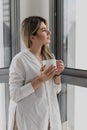 Young beautiful woman near window with cup of coffee or tea at home. Royalty Free Stock Photo