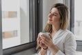 Young beautiful woman near window with cup of coffee or tea at home. Royalty Free Stock Photo