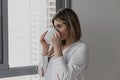 Young beautiful woman near window drinking cup of coffee or tea at home. Royalty Free Stock Photo