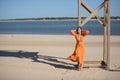 Young and beautiful woman in an orange dress, leaning on a wooden pole, hands on her head, looking at infinity, relaxed and calm, Royalty Free Stock Photo