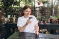 Young beautiful woman with paper white cup of coffee sitting at summer rustic cafe. Mockup. Female hand with disposable