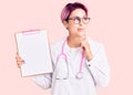 Young beautiful woman with pink hair wearing doctor stethoscope holding clipboard with medical report serious face thinking about Royalty Free Stock Photo