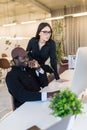 Young beautiful woman pointing at laptop with smile and discussing something with her african coworker while standing at office Royalty Free Stock Photo