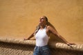 Young and beautiful woman, with ponytail, wearing a white top and jeans, with her eyes closed, leaning against a wall, relaxed, Royalty Free Stock Photo