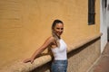 Young and beautiful woman, with ponytail, wearing a white top and jeans, smiling happily, leaning against a wall, relaxed, Royalty Free Stock Photo