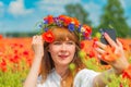 Young beautiful woman with a poppy wreath on the head taking selfie in the field on a summer day.
