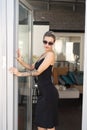 young beautiful woman posing in a black short dress near the glass door