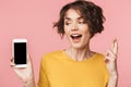 Young beautiful woman posing isolated over pink wall background using mobile phone showing display and hopeful please gesture