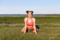 Young beautiful woman practicing yoga asana of a Simhasana lion pose on green grass near the lake