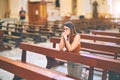 Young beautiful woman praying on her knees in a bench at church