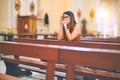 Young beautiful woman praying on her knees in a bench at church