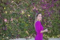 Young and beautiful woman in a purple dress, looking at the camera, posing with bougainvillea flowers in the background of the Royalty Free Stock Photo