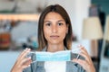 Young beautiful woman putting on an hygienic mask to prevent others from a virus while looking at camera in the home