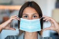 Young beautiful woman putting on an hygienic mask to prevent others from a virus while looking at camera in the home