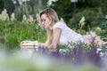 Young beautiful woman reading a book lying on the bench around the grass and flowers at summer day Royalty Free Stock Photo