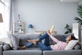 Young beautiful woman is reading a book while lying on a sofa in the living room