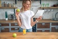 Young beautiful woman is reading her morning press and smiling while drimking orange juice in the kitchen. wearing white shirt Royalty Free Stock Photo