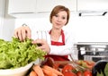 Young beautiful woman in red apron at home kitchen preparing vegetable salad bowl smiling happy Royalty Free Stock Photo