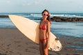 Young beautiful woman in red bikini and sun glasses holds in hands a surf on the ocean beach at sunset. Royalty Free Stock Photo