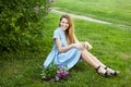 Young beautiful woman with red hair sits on a grass under the lilac tree and enjoys her life Royalty Free Stock Photo