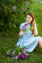 Young beautiful woman with red hair sits on a grass under the lilac tree and enjoys her life Royalty Free Stock Photo