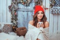 Young beautiful woman in red hat and cozy blanket drinking cup of coffee or cacao while sitting home by the window. Blurred winter Royalty Free Stock Photo