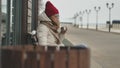 Young beautiful woman in a red hat wearing sporty warm clothes and rollers, sitting on a wooden bench drinking tea from Royalty Free Stock Photo