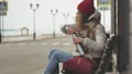 Young beautiful woman in a red hat wearing sporty warm clothes and rollers, sitting on a wooden bench drinking tea from Royalty Free Stock Photo