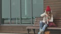 Young beautiful woman in a red hat wearing sporty warm clothes and rollers, sitting on a wooden bench drinking tea from Royalty Free Stock Photo