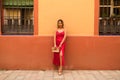 young beautiful woman in a red silk dress holds a pink handbag in her hands. The woman is leaning against a red and yellow wall in Royalty Free Stock Photo