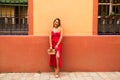 young beautiful woman in a red silk dress holds a pink handbag in her hands. The woman is leaning against a red and yellow wall in Royalty Free Stock Photo