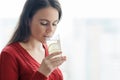 Young beautiful woman in red sweater with glass of water with lime, woman stands near window in skyscraper on cloudy day. Healthy Royalty Free Stock Photo