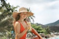 Young beautiful woman in a red swimsuit and a straw hat enjoying summer vacation, beach relax, summer in tropics Royalty Free Stock Photo