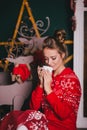 Young beautiful woman in a red warm pajamas with scandinavian ornaments sitting near decorative fireplace and drinking hot cocoa Royalty Free Stock Photo