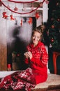 Young beautiful woman in a red warm pajamas with scandinavian ornaments sitting near decorative fireplace and drinking hot cocoa Royalty Free Stock Photo