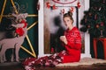 Young beautiful woman in a red warm pajamas with scandinavian ornaments sitting near decorative fireplace and drinking hot cocoa Royalty Free Stock Photo