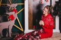 Young beautiful woman in a red warm pajamas with scandinavian ornaments sitting near decorative fireplace and drinking hot tea Royalty Free Stock Photo