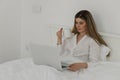 Young beautiful woman relaxing and drinking cup of hot coffee or tea using laptop computer on the bed in the bedroom. Royalty Free Stock Photo