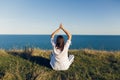 Young beautiful woman relaxing and practicing yoga on beach, sitting in grass, meditating and listening to sea waves. Hipster girl Royalty Free Stock Photo