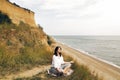 Young beautiful woman relaxing and practicing yoga on beach, sitting in grass and sand, meditating and listening to sea waves. Royalty Free Stock Photo