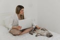 Young beautiful woman relaxing using laptop computer and stroking her gray Maine Coon cat in the bedroom. Working from home. Royalty Free Stock Photo