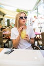 Young beautiful woman in round sunglasses with cocktail at the terrace of cafe having fun Royalty Free Stock Photo