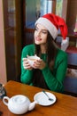 Young beautiful woman in Santas hat drinking tea in cafe Royalty Free Stock Photo