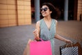 Young beautiful woman shopaholic walks out the shopping center with a pack of bags with purchases. Pink shopper in the hand of an