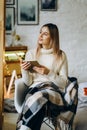 A young beautiful woman sits in a chair, covered with a blanket, reading a book near the window on Christmas Eve. Royalty Free Stock Photo