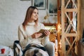 A young beautiful woman sits in a chair, covered with a blanket, reading a book near the window on Christmas Eve. Royalty Free Stock Photo