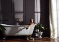 Young beautiful woman sitting in bathroom near expensive bathtub bath looking at the corner on dark Royalty Free Stock Photo