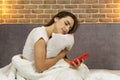 A young beautiful woman is sitting on the bed hugging a pillow and looking into the phone Royalty Free Stock Photo